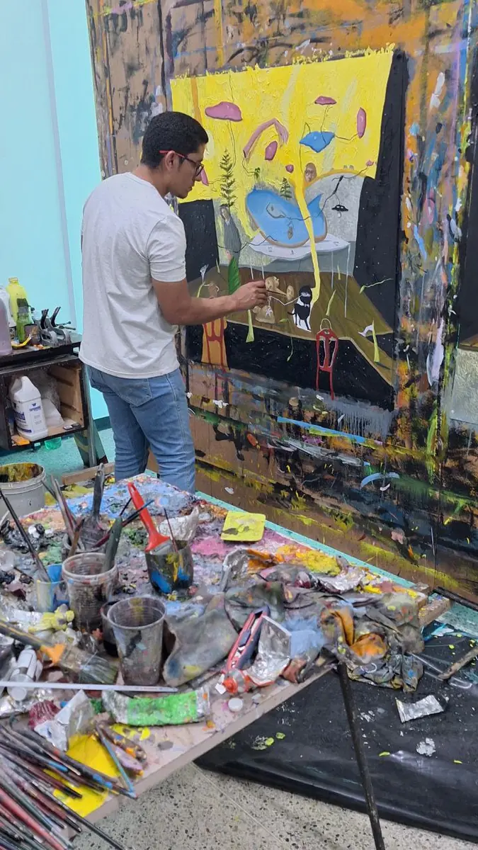 Galué painting a yellow canvas, the floor covered with materials